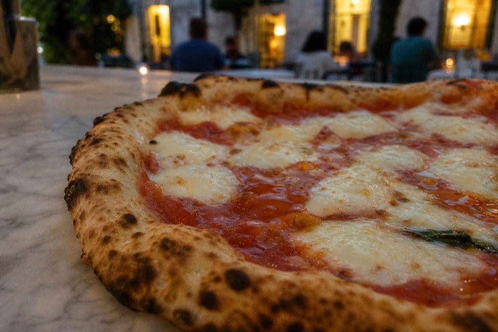 Close-up of a soft pizza centre with pooled tomato and melted mozzarella beside a puffed blistered crust rim on marble