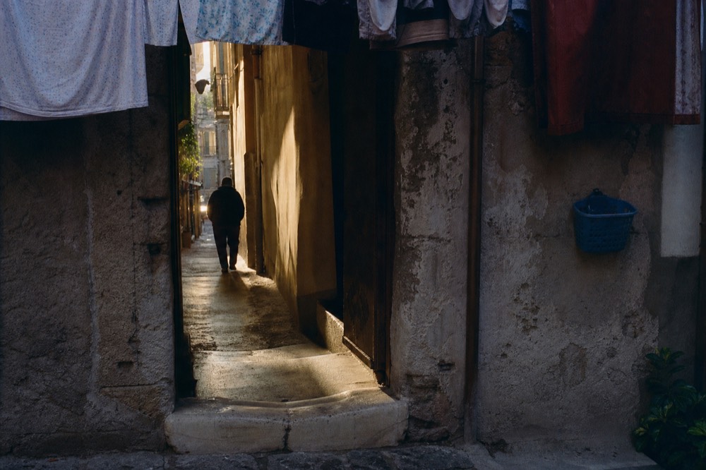 Weathered stone doorway of an old Naples alley with hanging laundry above and a pale marble threshold worn into a dip